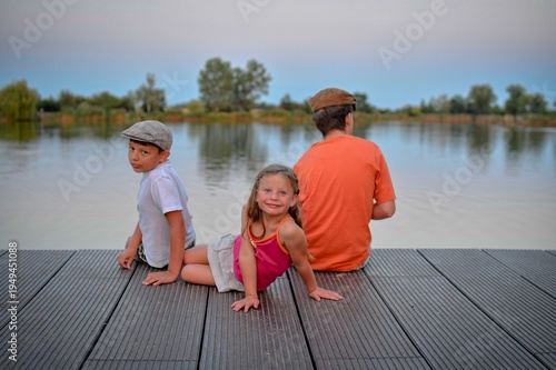 A group of young children sit on a wooden pier by a lake. The young children look toward the future. The concept of summer, holidays, and a carefree childhood. Summer and childhood concept. Children..