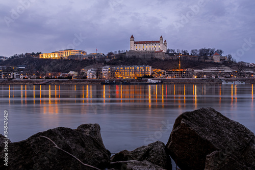 Photography Bratislava Castle at dusk above the Danube with city lights in Slovakia