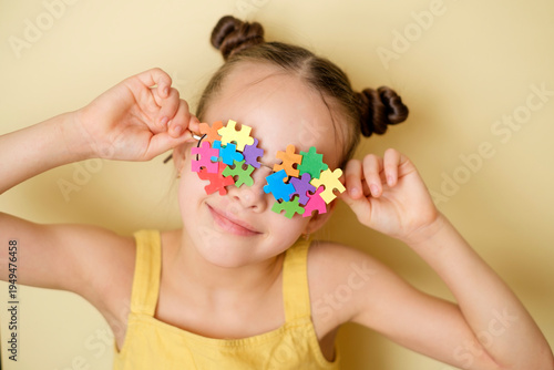 A happy, cheerful Girl with glasses decorated with colorful puzzle pieces. A sign symbolizing education and awareness about autism