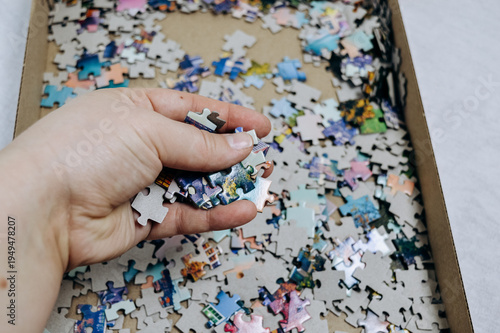 Hand taking jigsaw puzzle pieces from box, close up. Home leisure activity, puzzle game, concentration task, family entertainment, hobby and relaxation concept.