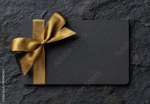 Black card with gold ribbon on a textured black slate background, gift or invitation