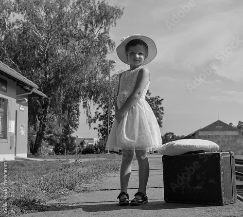 Young girl in a dress and hat with a suitcase at a train station, vintage style