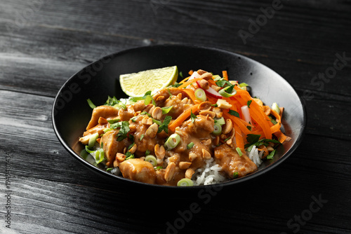 Chicken Satay with rice, roasted peanuts and greens in a black bowl