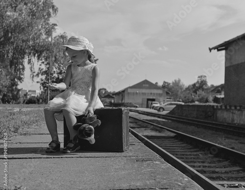 Young girl with suitcase and teddy bear waiting on a train platform