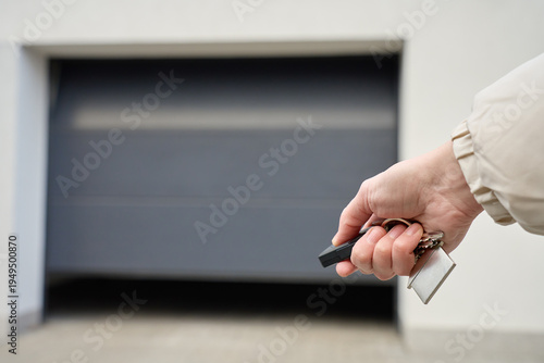 Closeup of hand holding garage remote and keys in front of closed garage door