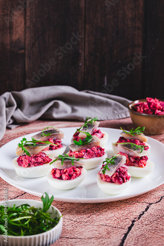 Egg halves stuffed with herring under a fur coat on a plate on the table vertical view