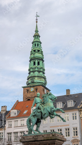 Photography Absalon's statue stands in Hojbro Plads, Copenhagen with a tall spire in the background
