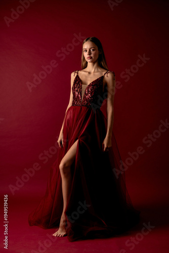 Model poses in red dress against simple background in studio setting