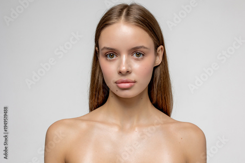Model poses in plain background with natural makeup and long hair for beauty shoot