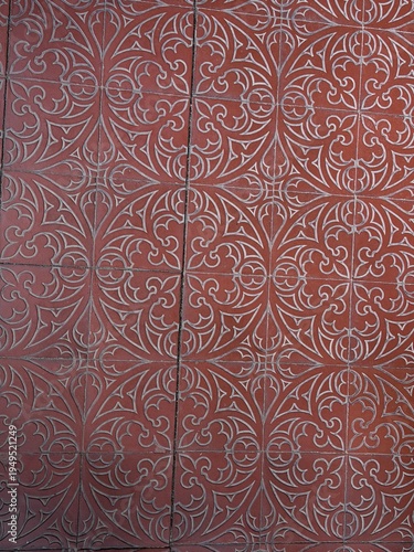 Red ornamental floor tiles with repeating Gothic floral pattern, forming a symmetrical vintage background with decorative geometric lines and historic architectural character.