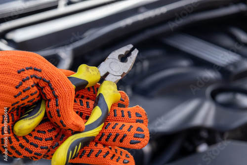Fotografija Brightly gloved hands grip pliers as a mechanic focuses intently on engine compo