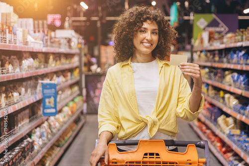 Slika na platnu Smiling woman purchasing products at the supermarket, holding a blank payment ca
