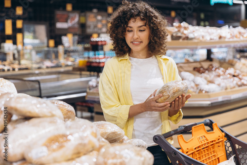 Foto Young woman shopping for fresh bread in a modern supermarket, choosing items fro