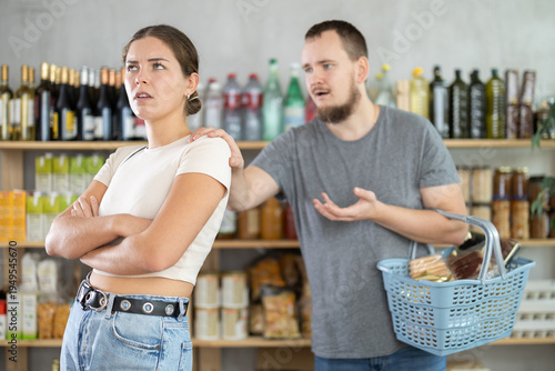 фотографія Angry girl turned away from husband during quarrel, he wants to make peace after quarrel and calms his wife, pats her on shoulder