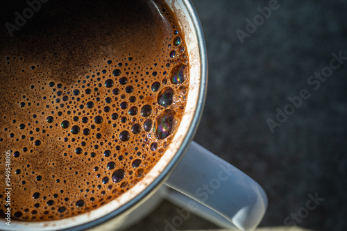 Top view of a cup of black coffee with foam on a textured stone surface. Moody high contrast lighting with dramatic diagonal shadow. Minimalist coffee break concept