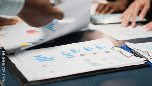 Фотография Multiethnic forecasting team reviewing report files during important meeting, updating project agenda and discussing business development with shareholders in office after hours