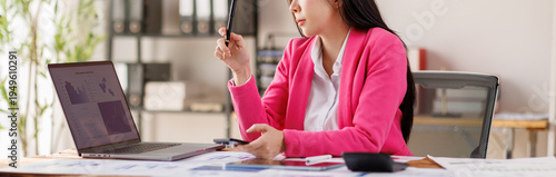 A focused woman in a pink blazer is analyzing data on a laptop, surrounded by documents and tools, demonstrating determination and professionalism in her workspace. Free Download A focused woman in a pink blazer is analyzing data on a laptop, surrounded by documents and tools, demonstrating determination and professionalism in her workspace. - GFXLoad