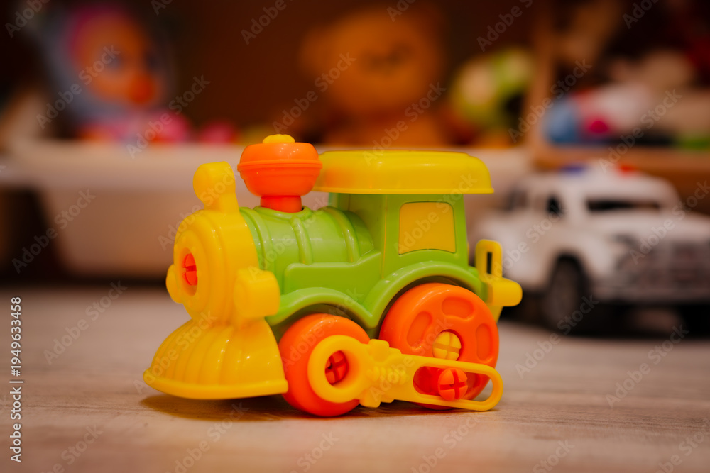 Naklejka premium Colorful plastic toy train standing on the floor in a child room. Locomotive model for play. Childhood fun, imagination, creative development and early education for toddler concept.