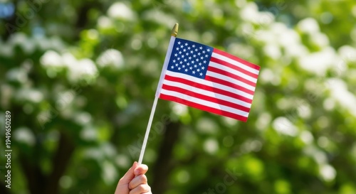 Child's hand holding small american flag with green trees
