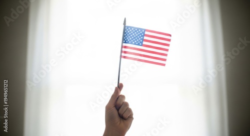 Hand holding american flag against bright window light, patriotism concept