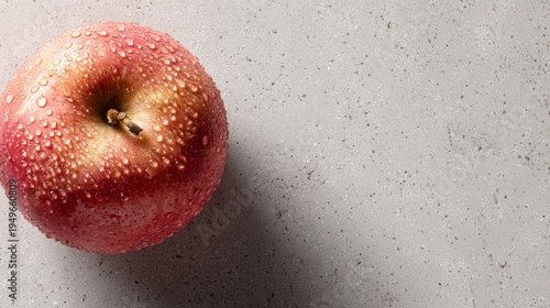 A ripe red apple with water drops on a textured surface