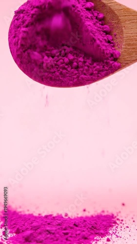Wooden spoon holding vibrant pink powder with particles falling