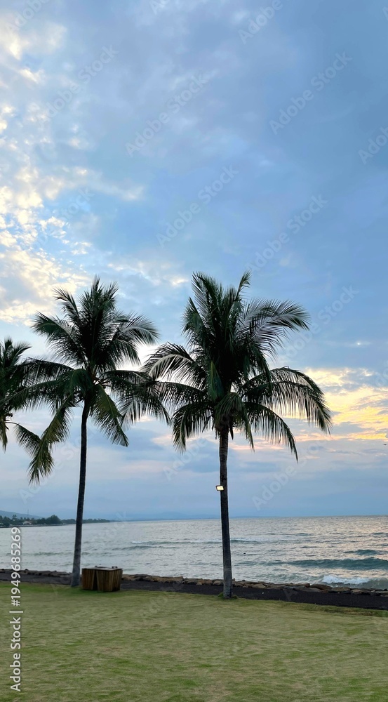 Fototapeta premium Beachside view with coconut palm trees swaying by the shore, clear sky and ocean creating a relaxing tropical coastal atmosphere perfect for travel escape.