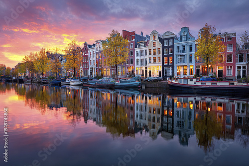 Amsterdam canal panorama with Dutch houses and boats at sunset reflects colorful sky and autumn trees, creating peaceful and picturesque urban scene by water