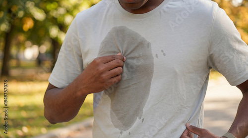 A man pulling on his heavily sweaty t-shirt after a vigorous outdoor workout session.
