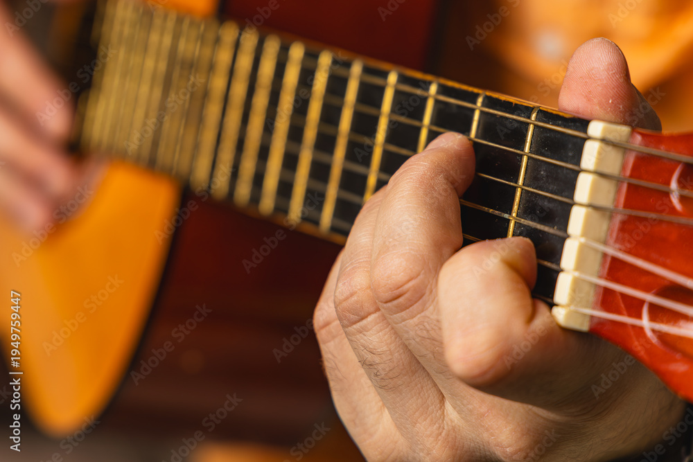 Fototapeta premium Man plays acoustic guitar indoors during evening