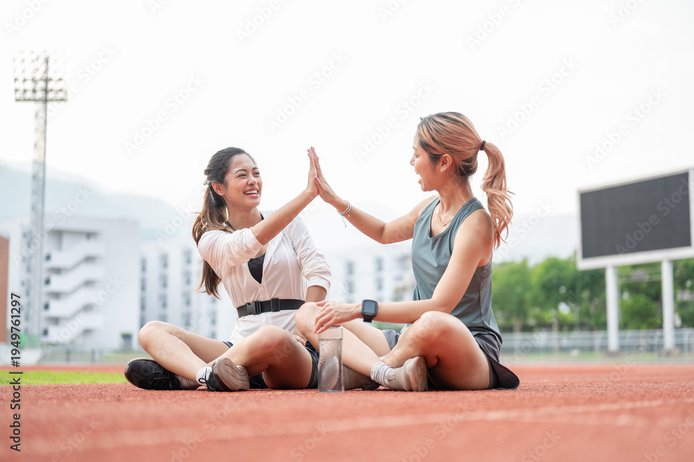 Obraz premium Asian woman clapping hands high five with friend while sitting resting on running track in stadium.