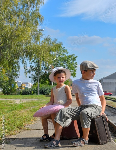 Adorable little girl and boy on a railway station, waiting for the train with vintage suitcase. Traveling, holiday and chilhood concept. Travel insurance concept. Travel, tourism, summer vacation and