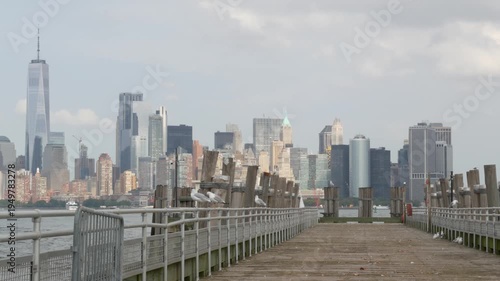 New York City Manhattan Downtown skyline from Liberty Island, United States. Financial District cityscape, World Trade Center skyscraper tower. Building architecture and wooden pier, seagull birds.