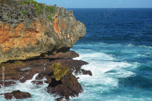 Stunning tropical coastline featuring rugged limestone cliffs and turquoise ocean waves crashing against rocks under a clear blue sky