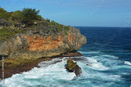 Stunning tropical coastline featuring rugged limestone cliffs and turquoise ocean waves crashing against rocks under a clear blue sky