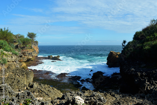 Stunning tropical coastline featuring rugged limestone cliffs and turquoise ocean waves crashing against rocks under a clear blue sky
