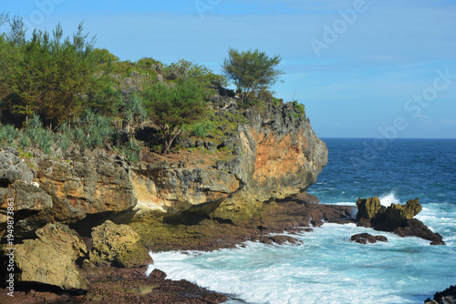 Rugged Limestone Sea Cliffs and Tropical Greenery Overlooking the Deep Blue Indian Ocean with Crashing White Waves at Nguluran Beach, South Coast of Yogyakarta