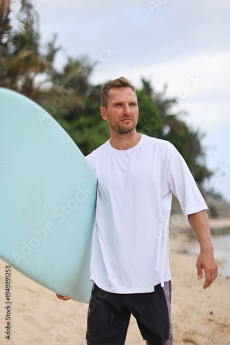Man Carrying Surfboard On Shoreline. Person In Plain Attire Walking Along Coast With Surfboard In Hand