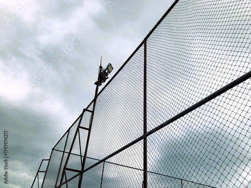 Stadium Floodlight and Fence Netting Against Cloudy Sky.