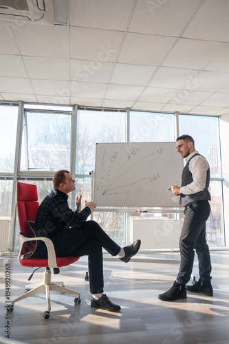 Two Caucasian men discussing work at a white board. 