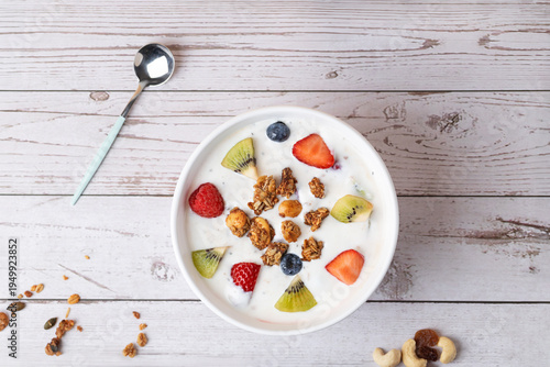 Top view composition of white kefir bowl with assorted fruits and granola on white wooden table. Clean and modern aesthetic. Copy space. Concept of nutrition and daily wellness