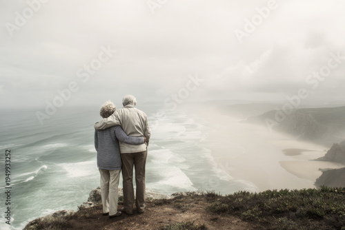 elderly couple standing on coastal cliffs looking at the horizon, arms around each other, wind gently blowing hair and clothing, dramatic yet natural seaside landscape, overcast soft diffused light,