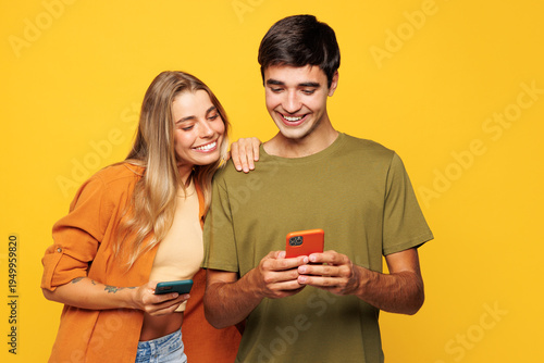 Young smiling happy couple two friends family man woman wear casual clothes hold in hand use mobile cell phone together chatting isolated on pastel plain light yellow color background studio portrait.