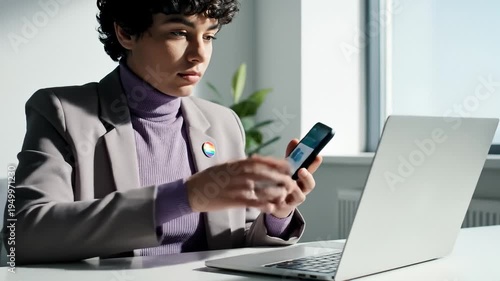 Person Wearing Pride Pin Working on Laptop and Using Smartphone in Office