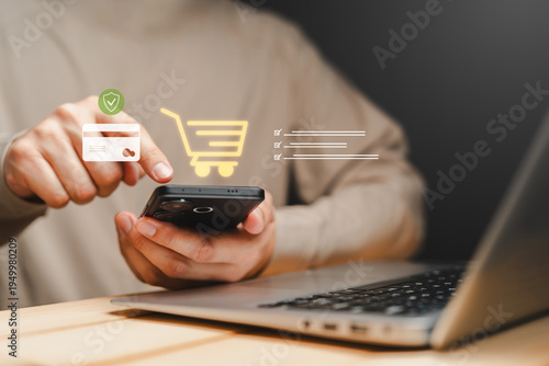 Person using smartphone for online shopping with digital cart and secure payment interface icons. Mobile e-commerce transaction, contactless payment and online purchase technology concept with laptop.