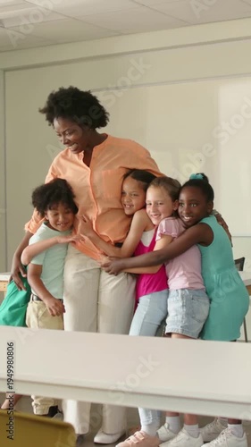 Vertical video: Moving in, kids hugging teacher in peach blouse showing care at school whiteboard