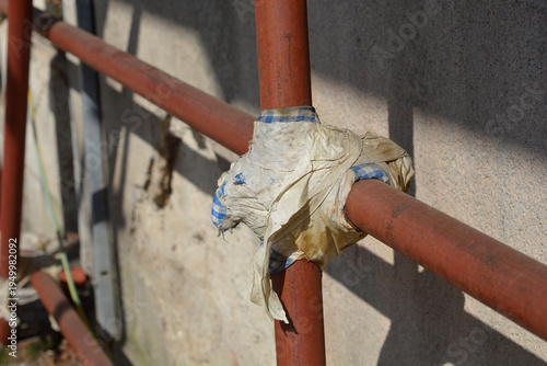 Two crossing brown painted metal pipes are joined together with a piece of old worn fabric at a construction site