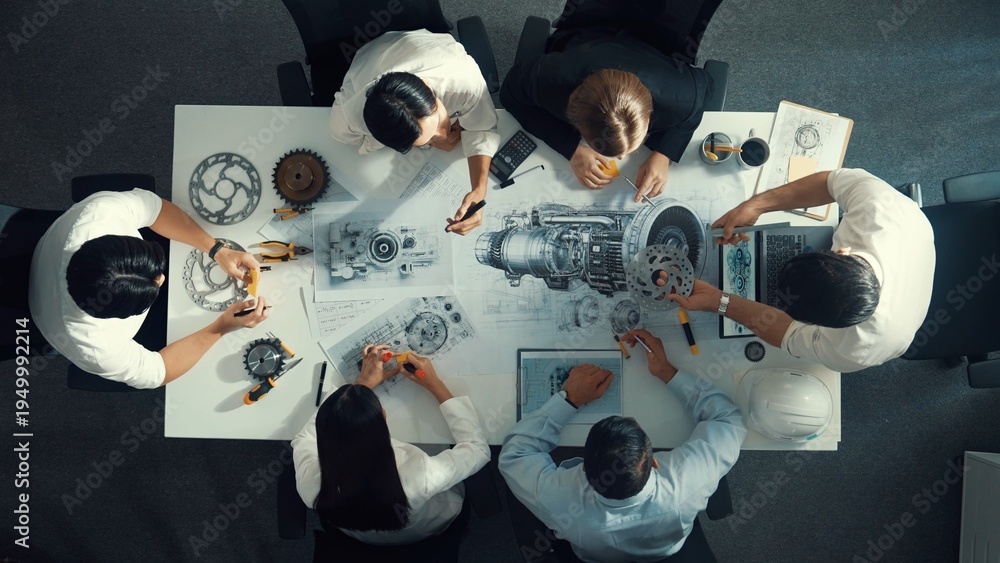 Obraz premium Top view of engineer pointing at turbine engine at meeting table with equipment. Aerial view of professional project manager talking and discussing about electronic generator system. Alimentation.