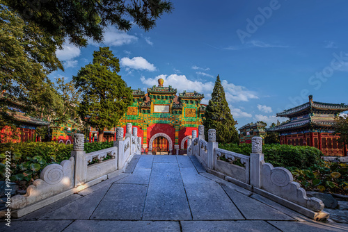 Entrance of Beijing Beihai Park Xiaoxitian Glazed Archway under clear sky with traditional architecture and lush greenery.