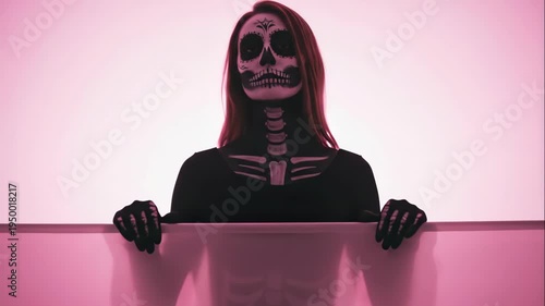 Woman with sugar skull face paint poses dynamically behind pink glowing panel. Day of the dead inspired mystical dance sequence in neon light for halloween or cultural performance